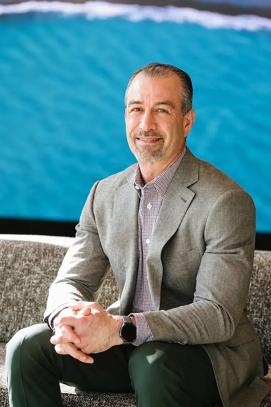 Dr. Jason Itri sitting on sofa with ocean background.